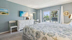 A bedroom with a bed, dresser, chairs, and a balcony with a view. - Oceanfront Getaway: Pool, Tennis & Walk to Pier + Putting Green (Cocoa Beach)