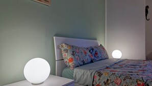 Une chambre à coucher avec un lit, une table de chevet dotée d’une lampe ronde et un téléphone fixé au mur.