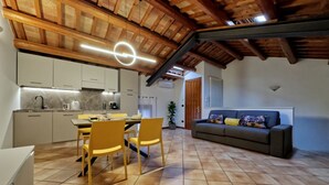 Une cuisine moderne avec des meubles blancs, un coin repas avec des chaises jaunes et un canapé gris dans l’espace salon.