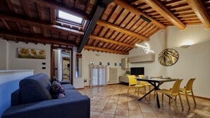 Un salon comprenant un canapé, une table à manger avec des chaises, un coin cuisine et un plafond avec des poutres en bois.