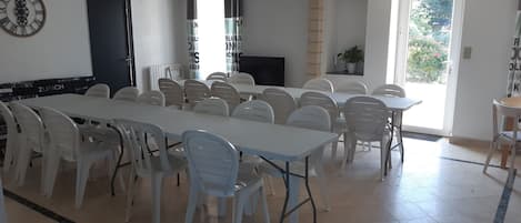 A spacious dining area with white tables and chairs, a clock on the wall, and a door leading outside.