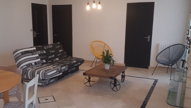 A living room with a sofa, a coffee table, a dining table with chairs, and a chair with a plant. - La Maison-Gîte-Family-Ensuite with Shower-Garden view (Beaulieu-sur-Layon)