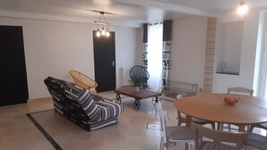 Een moderne woonkamer met een bank, eettafel, stoelen en een hanglamp.