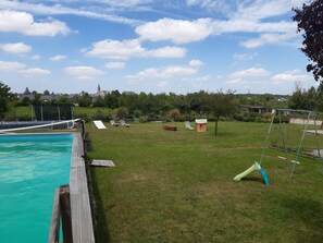 A backyard with a swimming pool, a wooden deck, and a grassy lawn with a swing set.