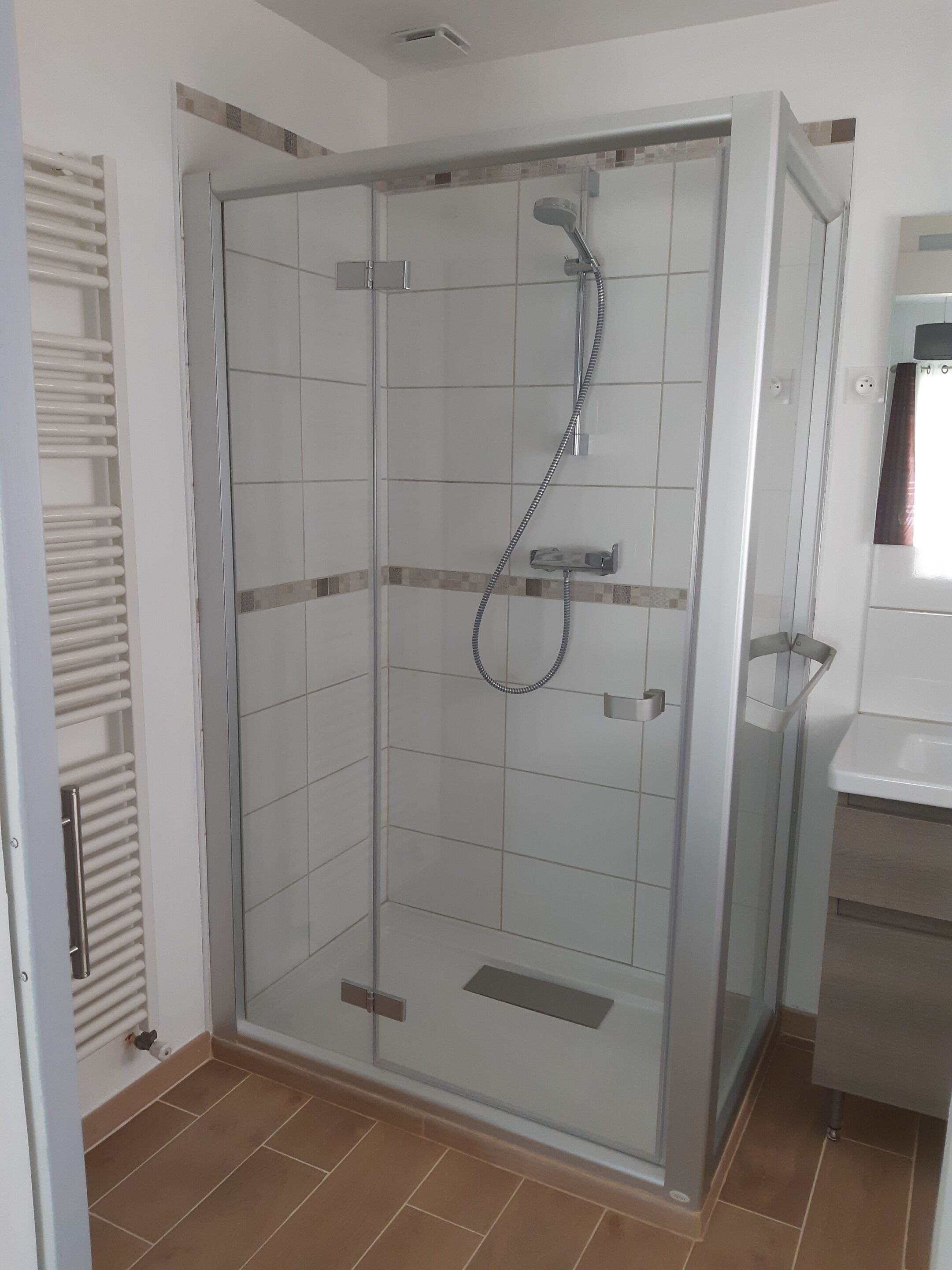 A glass-enclosed shower stall with a handheld showerhead and a wall-mounted faucet.