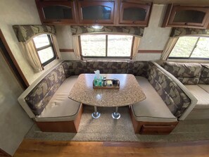 A cozy RV interior with a central seating area, a small table with a tray, and a window providing a view of the outdoors. - Mosquito Range Views! Nestled closely to many 14er’s!  (Hartsel)