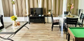 Una sala de estar con mesa de billar, televisión y comedor con sillas y mesa.
