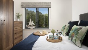 Un dormitorio con cama, ventana con vista a árboles, armario y mesita de noche con objetos decorativos.