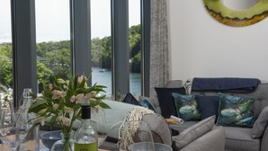 Una sala de estar moderna con vista a un lago, una mesa de vidrio con copas de vino y un sofá con almohadones decorativos.