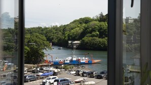 Vista de un puerto con un gran carguero amarrado, rodeado de exuberante vegetación y coches estacionados.