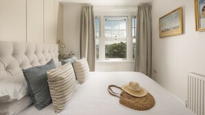 A bedroom with a tufted headboard, striped pillows, a woven bag, and a painting on the wall.
