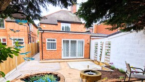 A brick house with a garden, a wooden fence, a bird bath, and a bench. - Luxury Family Apartment- Garden View (Leicester)
