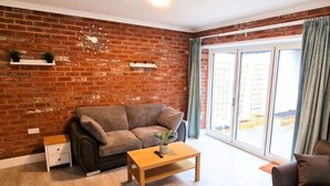 A living room with a brick wall, a sofa, a coffee table, and a window with curtains. - Luxury Family Apartment- Garden View (Leicester)
