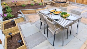Un patio con mesa lista para comer, rodeado de jardines elevados y una pequeña fuente.
