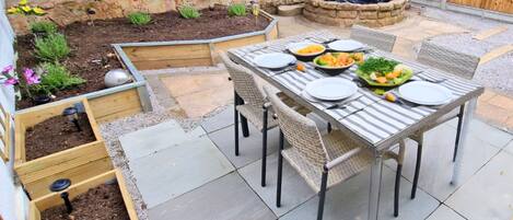 A patio with a table set for dining, surrounded by raised garden beds and a small water feature.