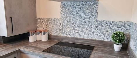 A modern kitchen with a built-in stove, stainless steel cabinets, and patterned backsplash tiles.