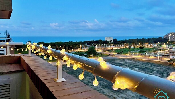 Varanda com luzes de corda e vista para o mar e a paisagem urbana.