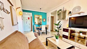 Uma sala de estar com sofá, mesa de centro, televisão e um espaço de refeições com cadeiras e mesa.