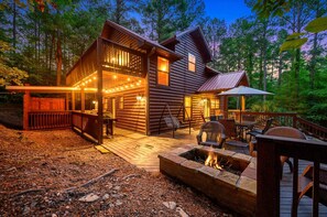 A log cabin with a deck, outdoor seating, and a fire pit.