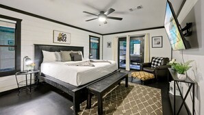 A modern bedroom with a large bed, a ceiling fan, a TV, and a window with a view. - Wild Oasis · New! Wild Oasis: Pool, Gameroom, Theatre, Hot Tub (Broken Bow)