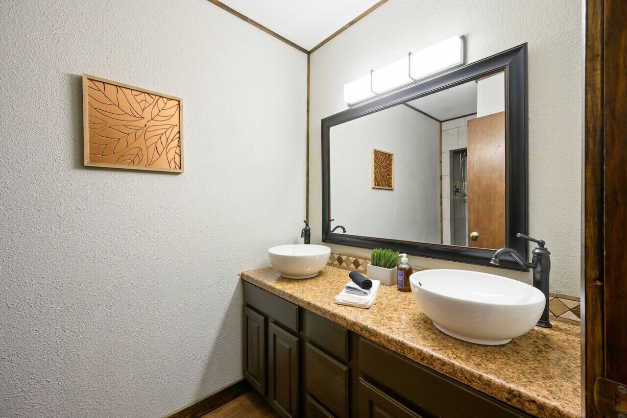 Un baño con un espejo grande, dos lavamanos, una toalla y una planta pequeña.