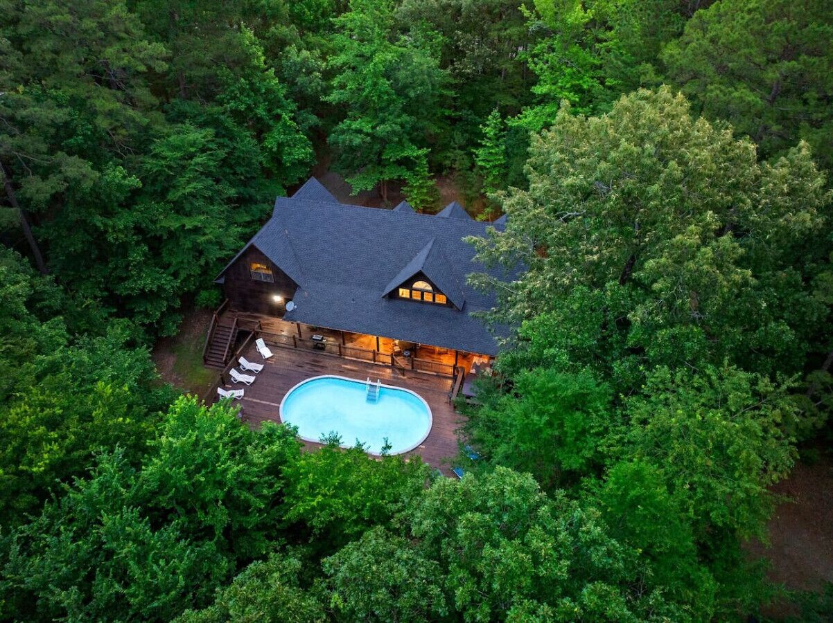 An aerial view of a lodge with a swimming pool surrounded by dense forest.