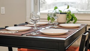 Mesa lista para comer con platos, vasos y cubiertos, con una planta en maceta y vistas al exterior.