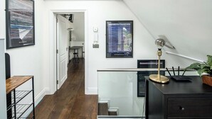 Un intérieur moderne avec un escalier, un bureau doté d’une lampe et des œuvres d’art encadrées accrochées aux murs.