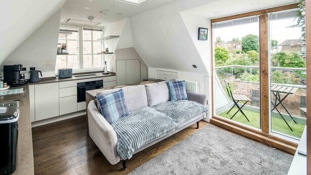 Un appartement moderne de style « loft », comprenant une cuisine, un canapé et une grande porte-fenêtre coulissante donnant sur un jardin.