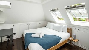 Une chambre à coucher avec un lit, des fenêtres de toit, un bureau et une table de chevet.