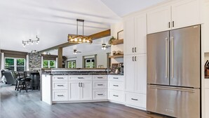Una cocina amplia con armarios blancos, un refrigerador de acero inoxidable y encimera de mármol.