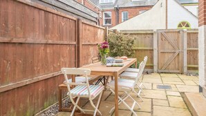 A wooden table with chairs in a backyard, surrounded by a wooden fence and a brick house in the background.