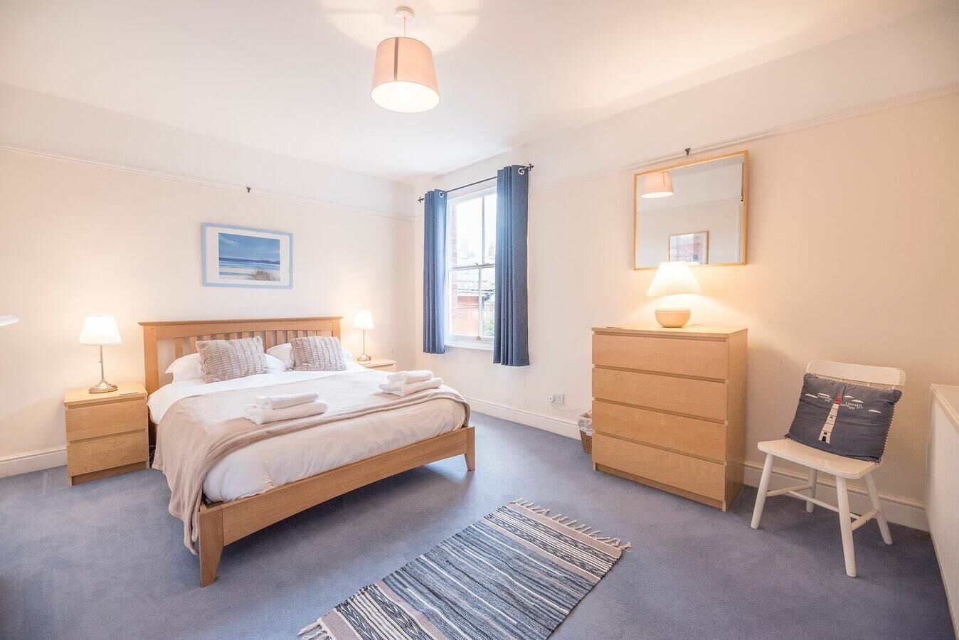 A bedroom with a bed, bedside tables, a dresser, a chair, a mirror, and a window with curtains.