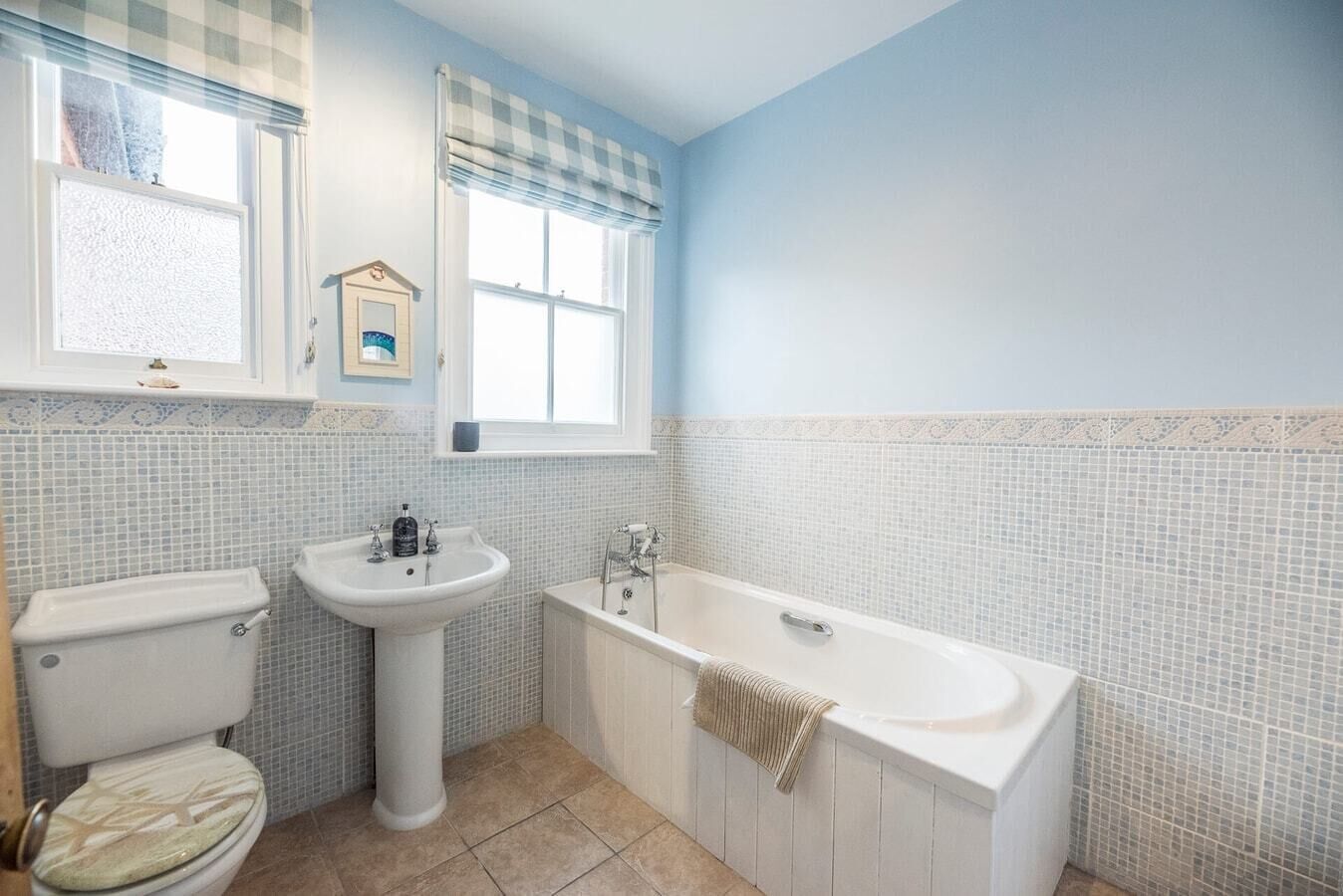 A bathroom with a toilet, sink, and bathtub, featuring blue walls and patterned tile flooring.