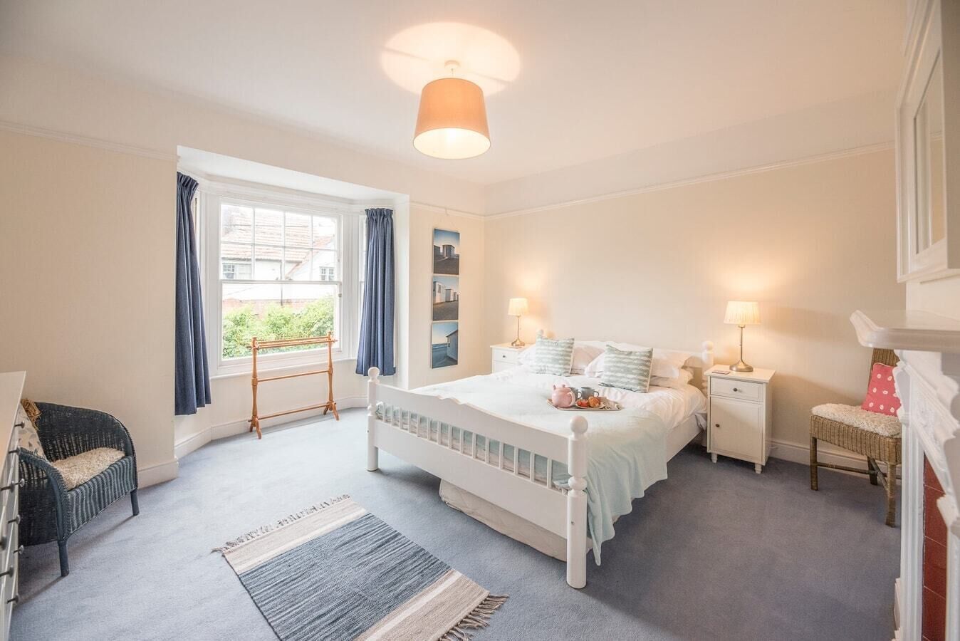 A bedroom with a large bed, bedside tables, a window with curtains, and a hanging light fixture.