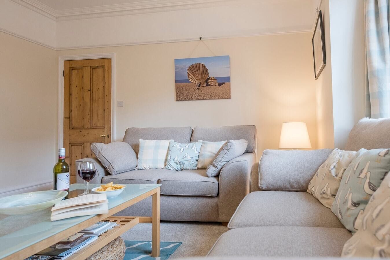 Ein gemütliches Wohnzimmer mit grauem Sofa, einem Holztisch und einer Lampe.