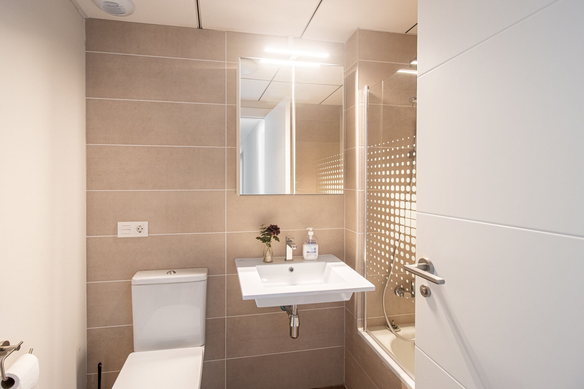 Ein modernes Badezimmer mit einem weißen Waschbecken, beigen Fliesen, einer Toilette und einer Duschkabine.
