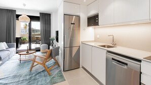A modern kitchen with stainless steel appliances, a dishwasher, and a dining area with a sofa and a round table. - Marinsa Beach Phase 2, 1 bedroom (Torrox)