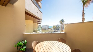 A balcony with a round wooden table and wicker chairs, a potted plant, and a view of buildings and palm trees. - Marinsa Beach Phase 2, 1 bedroom (Torrox)