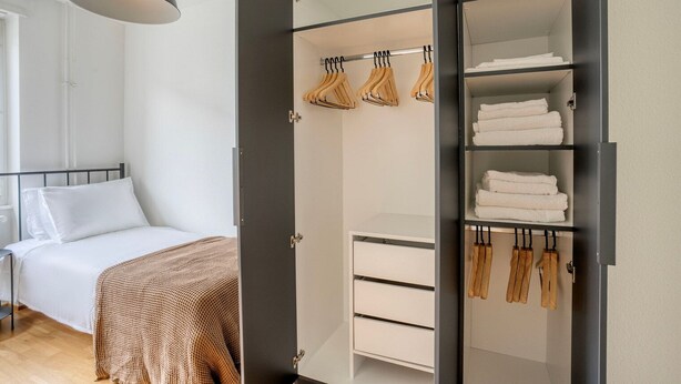 A bedroom with a bed, a wardrobe with hanging space, and a bedside table. - Clean Klybeck 3BR w/ Elevator & W/D, near River, by Blueground (Basel)