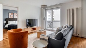 A modern living room with a sofa, a coffee table, a TV, and a view of the outside balcony. - Clean Klybeck 3BR w/ Elevator & W/D, near River, by Blueground (Basel)