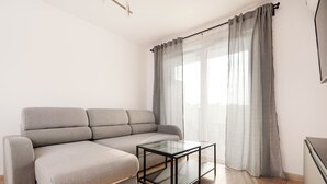 Una sala de estar moderna con un sofá seccional gris, una mesa de centro de vidrio y cortinas translúcidas.