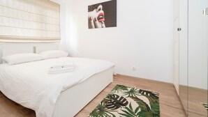 Un dormitorio con cama, ventana con persianas, un cuadro en la pared y suelo de madera.