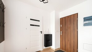 Un pasillo con piso de madera, una puerta blanca con líneas horizontales, un armario negro y otra puerta de madera.