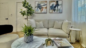 A living room with a beige sofa, a round coffee table with a marble top, a small potted plant, and abstract art on the wall. - 3 BR Cottage House Near Strip! (Las Vegas)