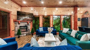 A cozy cabin interior with a stone fireplace, a blue sofa, a green sofa, and a white coffee table.