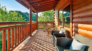 A wooden deck with wicker furniture and a view of a forested area.
