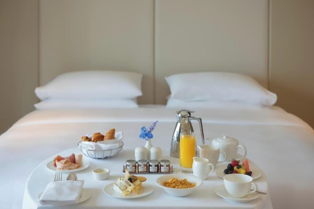 A neatly arranged breakfast buffet on a hotel bed with a pillow in the background.