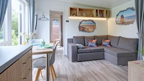 A modern living room with a grey sofa, wooden dining table, and a view of the outdoors through large windows. - Tiny Haus Anita by Interhome (Beilngries)
