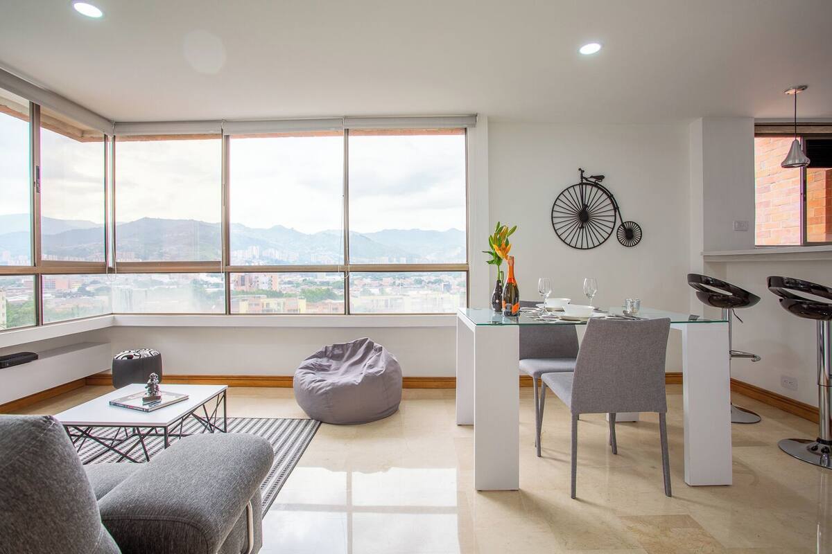 A modern living space with a dining area, a bean bag chair, and a view of a cityscape through large windows.